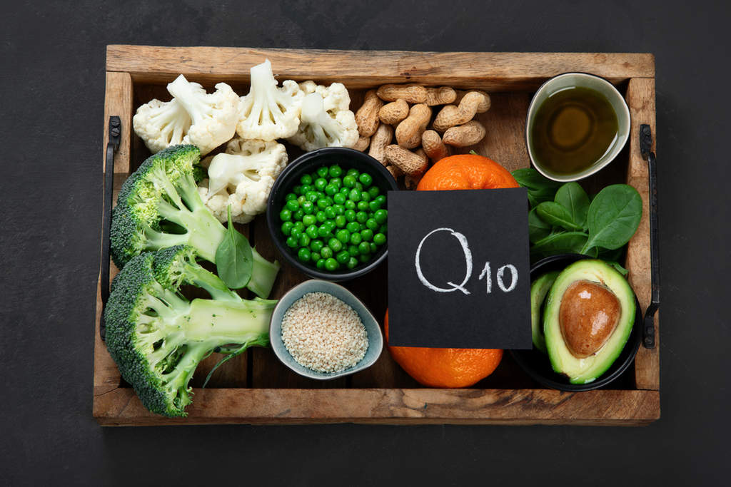 Uma caixa com alimentos como couve-flor, brócolis, ervilhas, tangerina, amendoim e abacate. E uma placa escrita "Q10" sobre eles, simbolizando onde encontrar coenzima q10